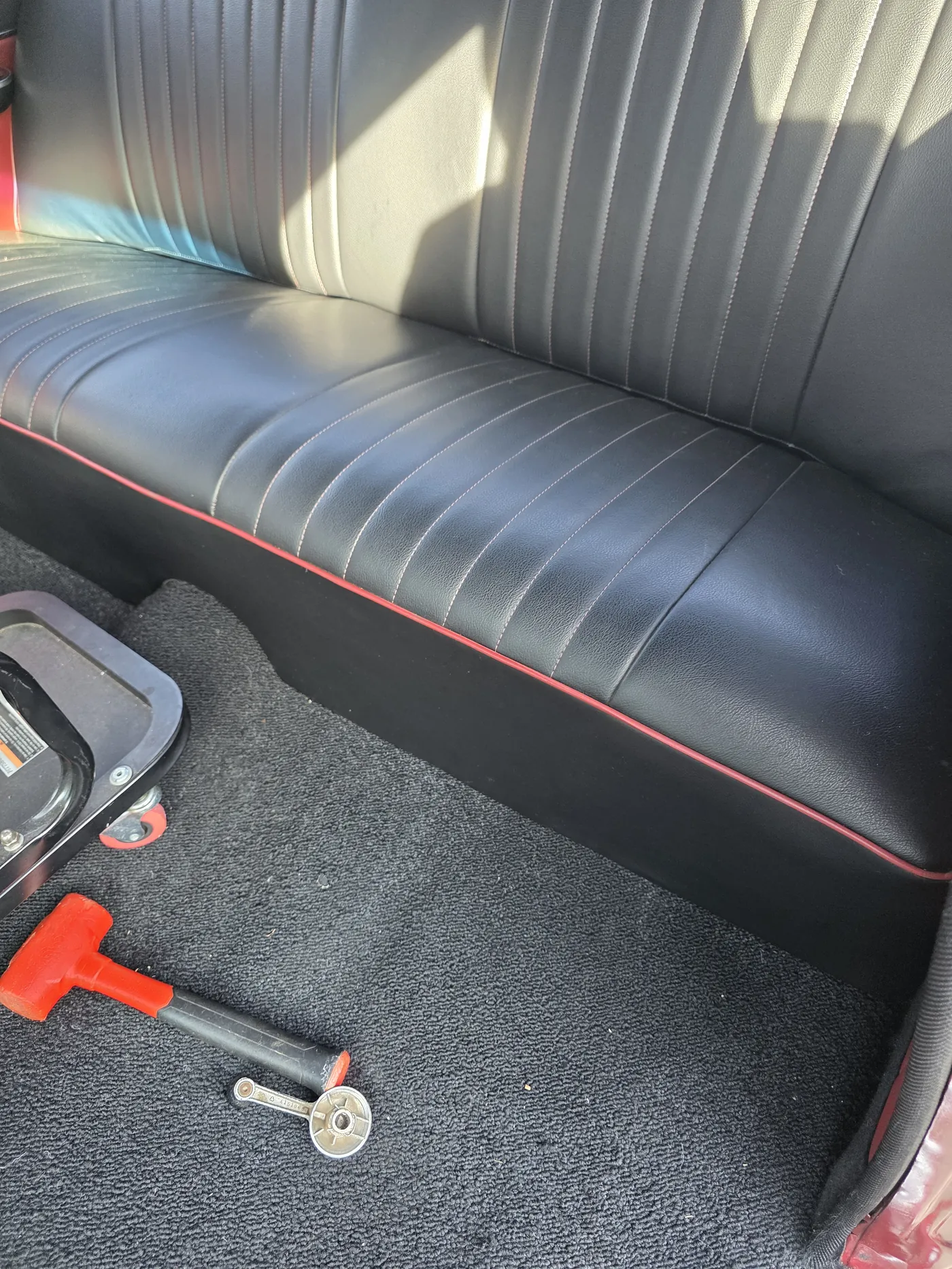 A black bench seat with red piping, photographed in the shop