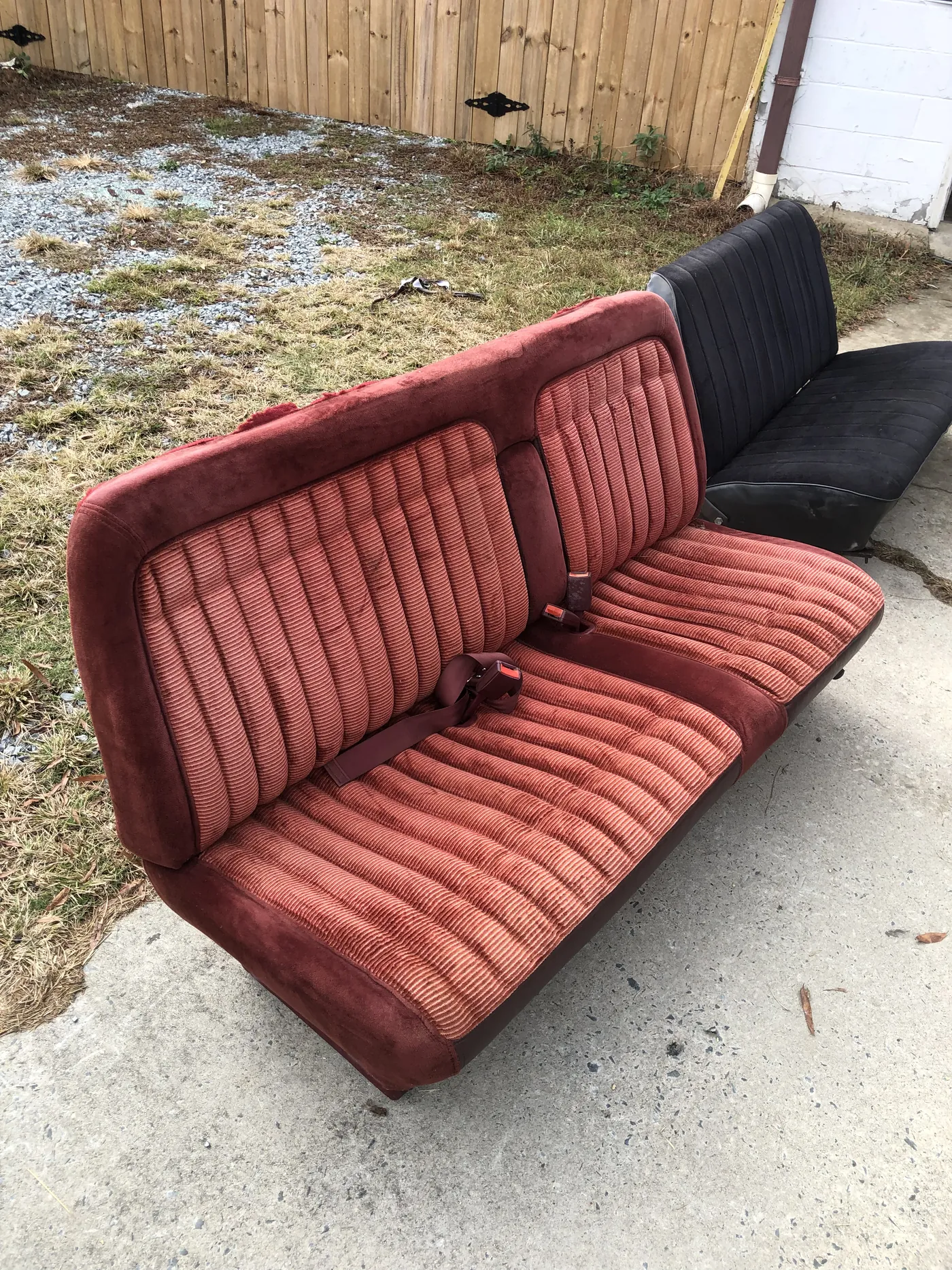 A finished bench seat recovered in red, outside the shop