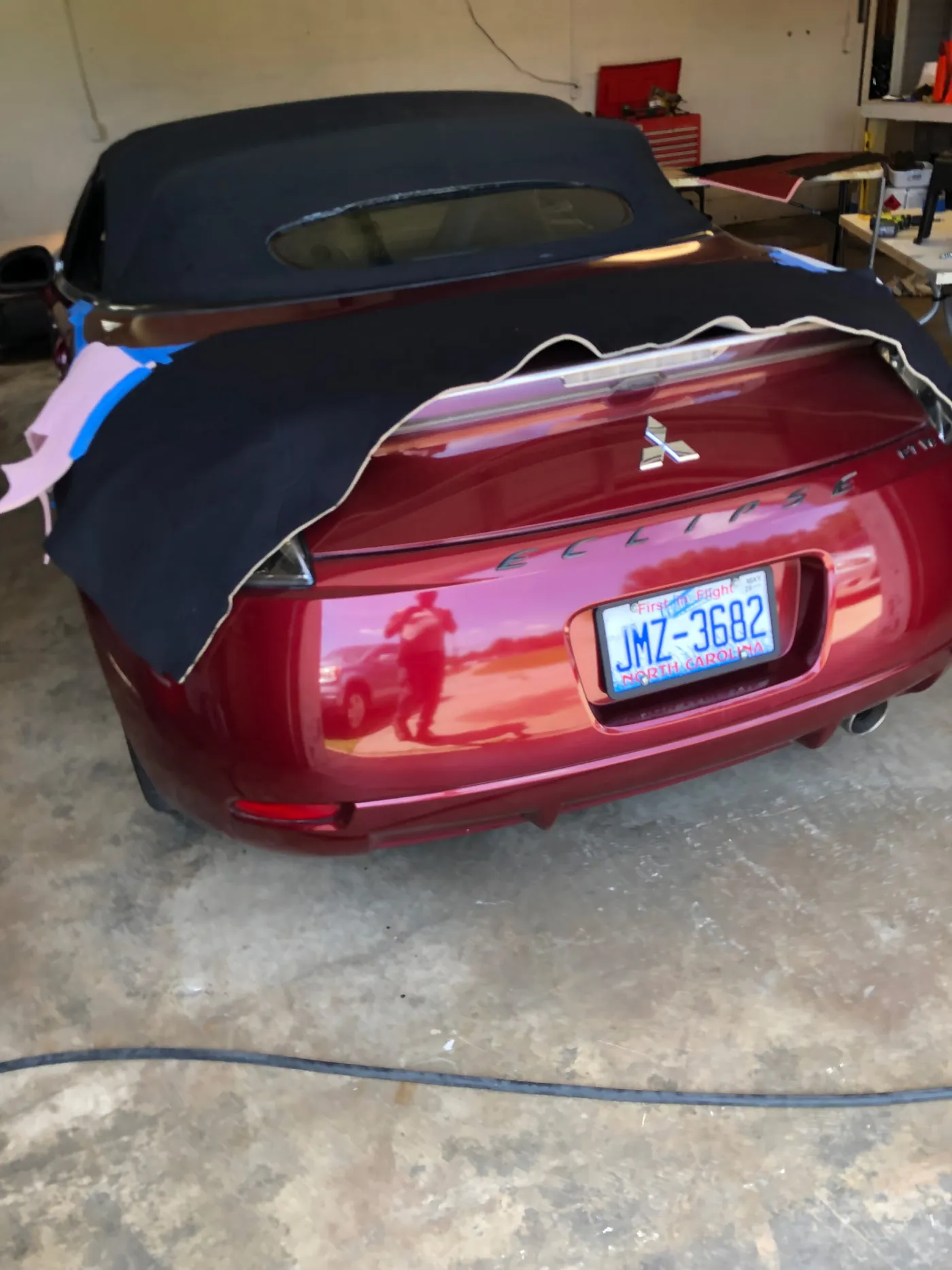 A red convertible in the shop with the old top off, laid back over the rear deck
